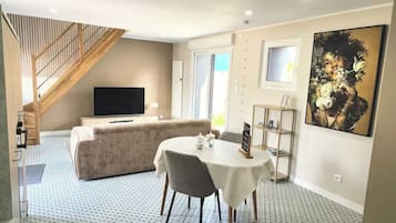 Ein Wohnzimmer mit einer Couch, einem Fernseher, einem Esstisch mit Stühlen, einer Treppe und einem großen Gemälde an der Wand.