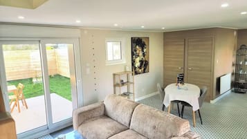 Ein Wohnzimmer mit einer Couch, einem Esstisch mit Stühlen, einer Glastür zu einer Terrasse und einem großen Gemälde an der Wand.