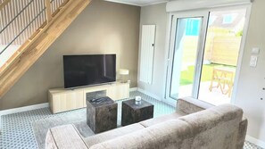 Una sala de estar con televisor, sofá, mesa de centro y una escalera.