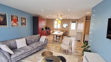 Ett vardagsrum med en grå soffa, en matplats med ett träbord och ett kök med röda skåp.