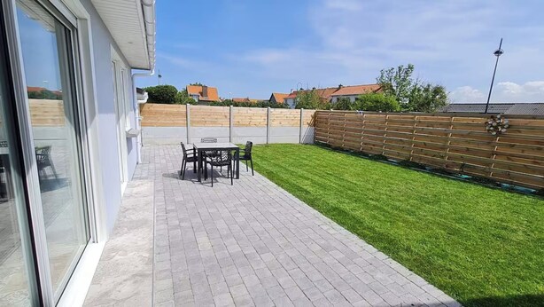 Een terras met een tafel en stoelen, een houten hek en een verzorgd gazon.
