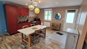 Een keuken met rode kastjes, een eettafel en een groot raam.