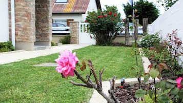 Een tuin met gazon, een roze bloem en een huis met bakstenen muren en een pannendak.