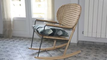 En gungstol med ett flätat ryggstöd och en kudde, placerad i ett rum med mönstrade golvplattor och ett vitt element.
