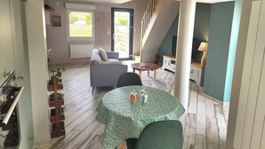 Een ruime woonkamer met een bank, een eettafel en een trap naar een hoger gelegen verdieping.