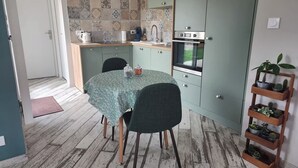 Een compacte keuken met een eettafel, stoelen, een inbouwoven en een plank met potplanten.