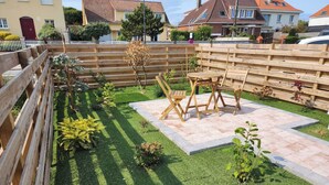 Een verzorgde achtertuin met een houten omheining, een terras met een tafel en stoelen, en diverse beplanting.