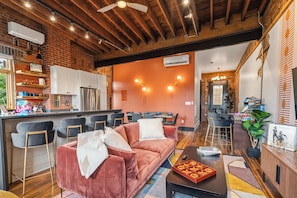 A modern living room with a red sofa, a coffee table, and a bar area with stools. - Dedicated Parking | King Bed | Arcade | Patio (Pittsburgh)