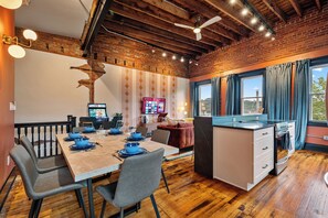 Een moderne keuken met een houten eiland, een eethoek met blauw servies en een bakstenen muur.