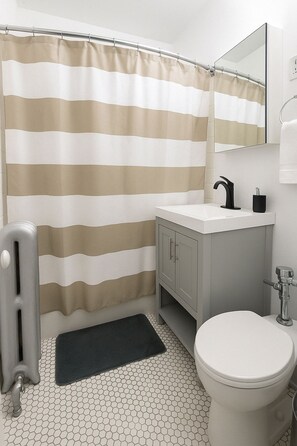 Een badkamer met een gestreept douchegordijn, een wit wastafelmeubel met een zwarte kraan, een toilet en een spiegel boven de wastafel.
