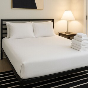 Een net opgemaakt bed met witte lakens, een zwart hoofdeinde en een stapel opgevouwen handdoeken aan de zijkant.
