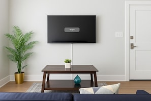 Een woonkamer met een flatscreen televisie aan de muur, een donker houten salontafel, een potplant en een bank.