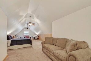 A spacious attic bedroom with a large bed, a beige sofa, and two ceiling fans.