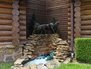 A log cabin with a stone waterfall feature and a deer sculpture.