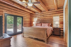 A log cabin bedroom with a bed, a nightstand, a ceiling fan, and a sliding glass door leading to an outdoor area.