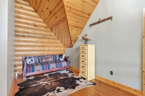 A bedroom with a sloped ceiling, a bed with a patterned bedspread, a dresser, and a cowhide rug.