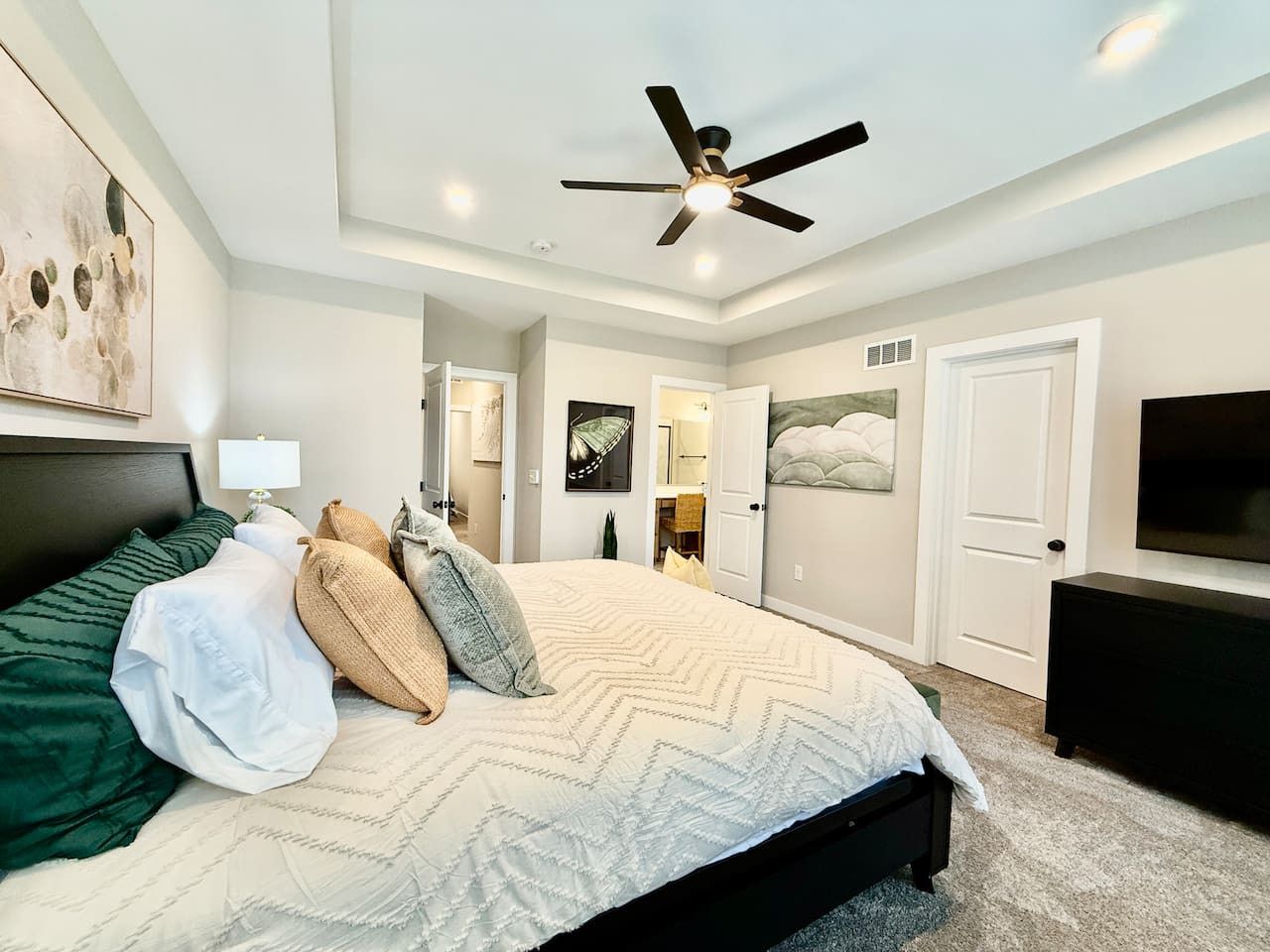 A bedroom with a bed, a ceiling fan, a TV, and a door leading to another room.