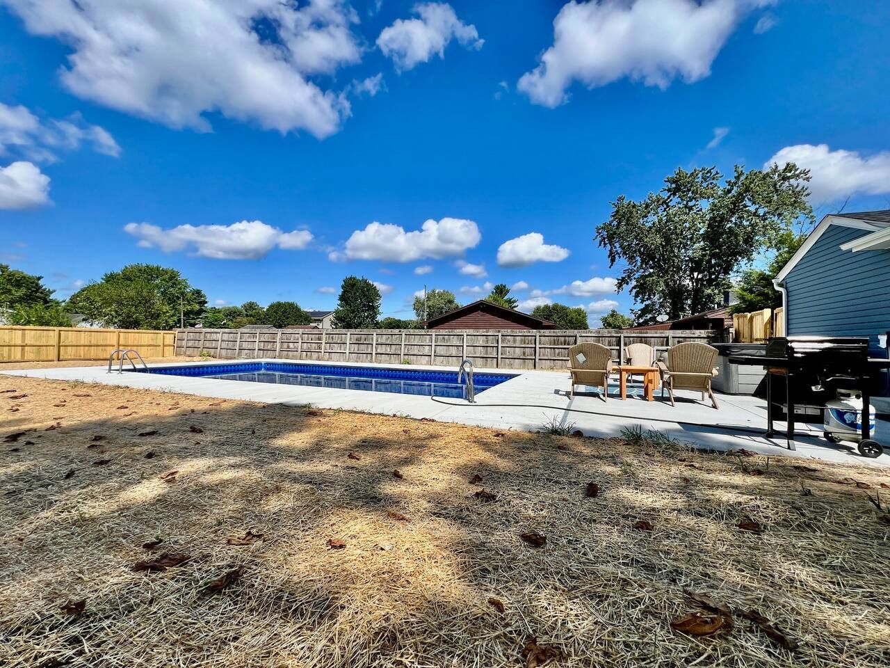 A backyard with a swimming pool, a wooden fence, and a covered patio area.
