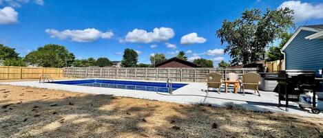 A backyard with a swimming pool, a wooden fence, and a covered patio area.