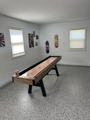 Una habitación con mesa de juego para rifa, dos ventanas con persianas y decoración en la pared.