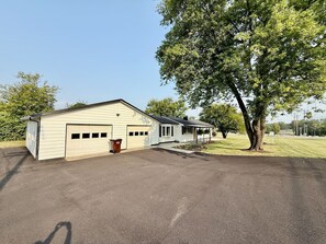 En etagers bygning med garage, en overdækket veranda og et stort træ foran.