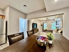 A modern kitchen with a dining area, a television, and a living room with a sofa and a plant.
