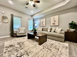 Una sala de estar con sofá, sillón, mesa de centro y ventilador de techo.