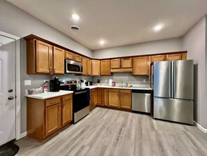 A modern kitchen with wooden cabinets, stainless steel appliances, and a light wood floor.