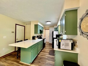 Une cuisine avec des meubles de couleur verte, un plan de travail blanc et un four à micro-ondes encastré.