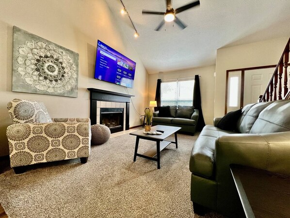 A living room with a fireplace, a television mounted on the wall, a ceiling fan, and a staircase.