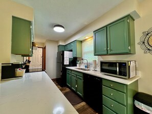 A kitchen with green cabinets, a white countertop, a microwave, and a sink.