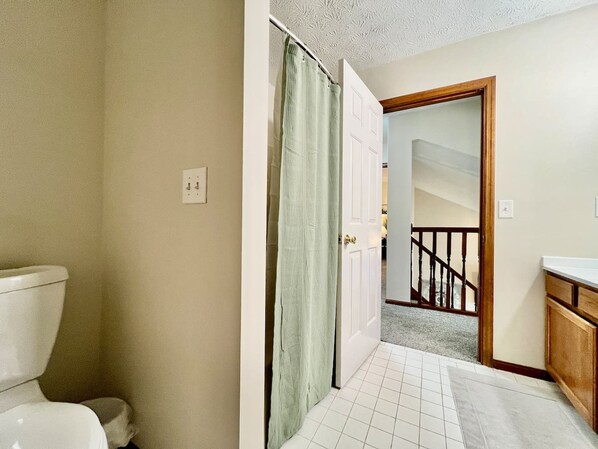 A bathroom with a toilet, a shower curtain, and a door leading to a staircase.