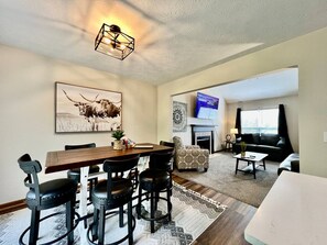A living room with a fireplace, a television, and a dining area with a wooden table and chairs.