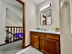 A bathroom with wooden cabinets, a white countertop, a mirror, and a small plant.