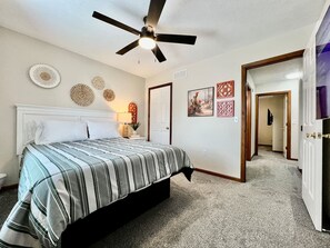 A bedroom with a bed, a ceiling fan, a nightstand, a lamp, and wall decor.