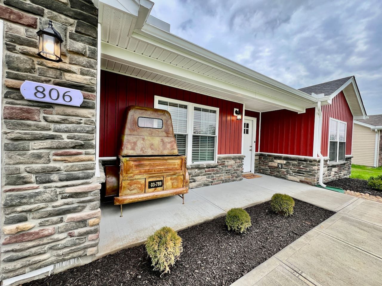 A house with a stone facade, a red door, and a vintage refrigerator in front.