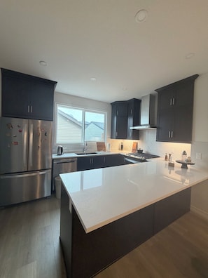 A modern kitchen with dark cabinetry, a stainless steel refrigerator, and a large island with a sink.