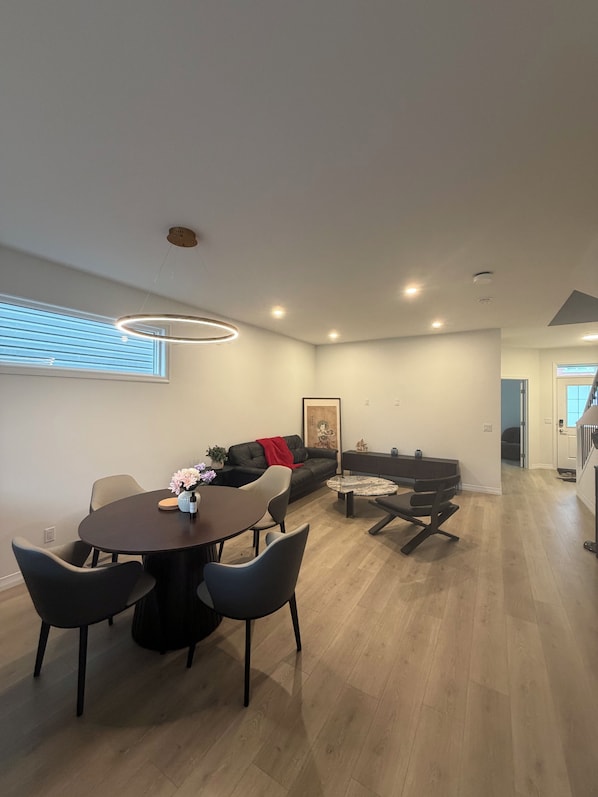 A modern living room with a dining area, a sofa, and a staircase leading to another level.