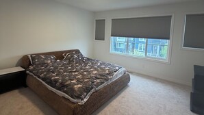 Een slaapkamer met een groot bed, een raam met zonwering, een plafondlamp en een vloerkleed.