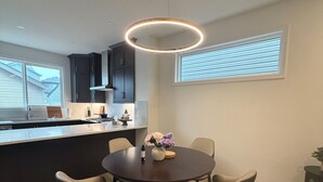 Et moderne køkken med mørke skabe, et rundt spisebord med stole og en hængende lampe.