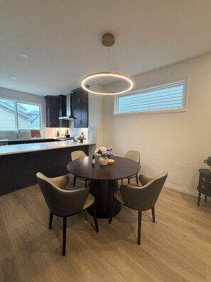 Una cocina moderna con armarios oscuros, una mesa redonda con sillas e iluminación colgante.