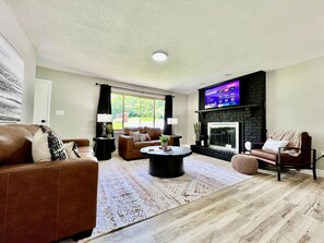 Un salon avec une cheminée, des canapés en cuir, une table basse et un téléviseur fixé au mur.