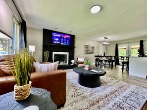 Una sala de estar moderna con chimenea, un televisor de pantalla plana y una zona de comedor con sillas y una mesa.