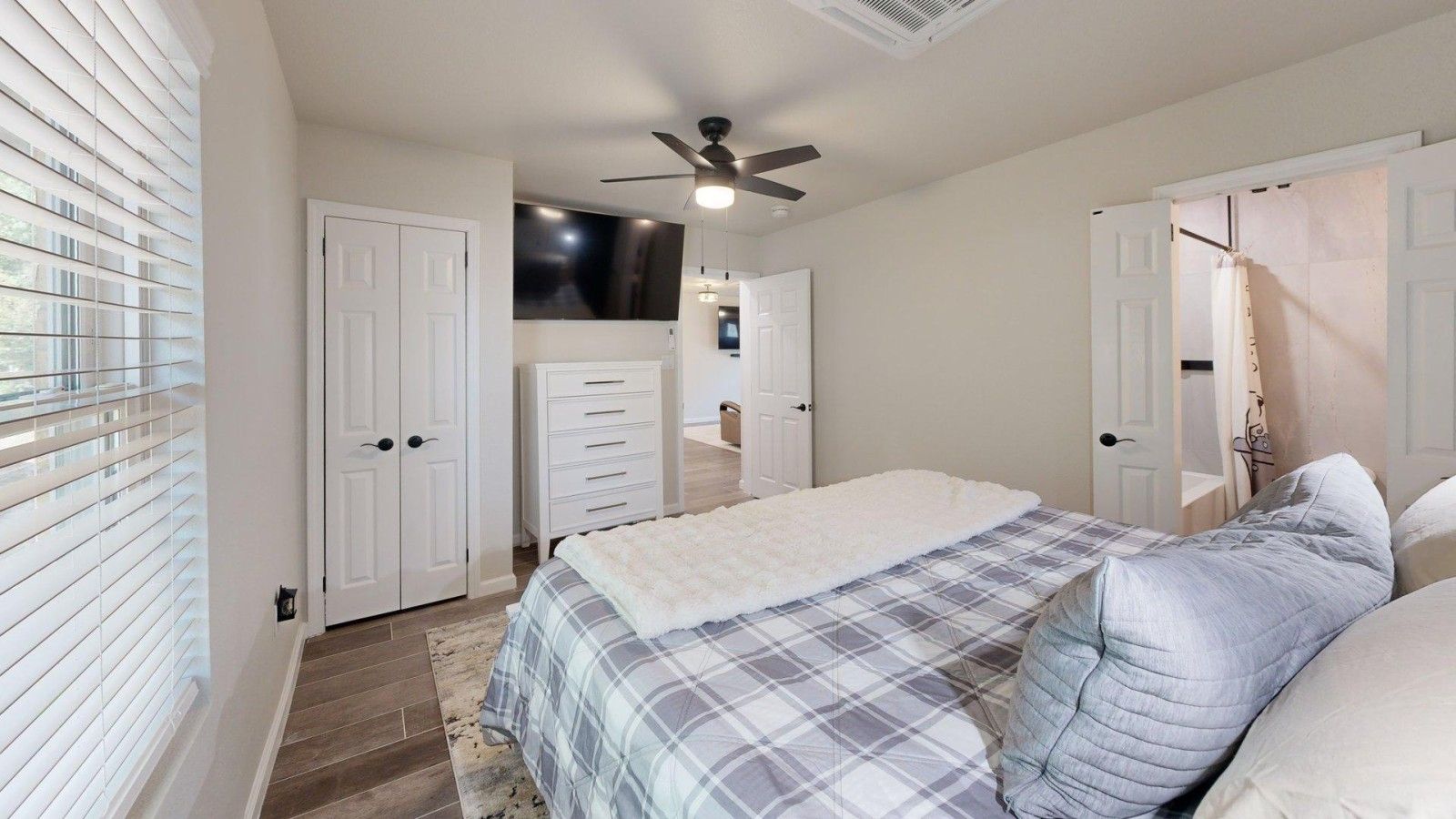 A bedroom with a bed, a ceiling fan, and a window with blinds.