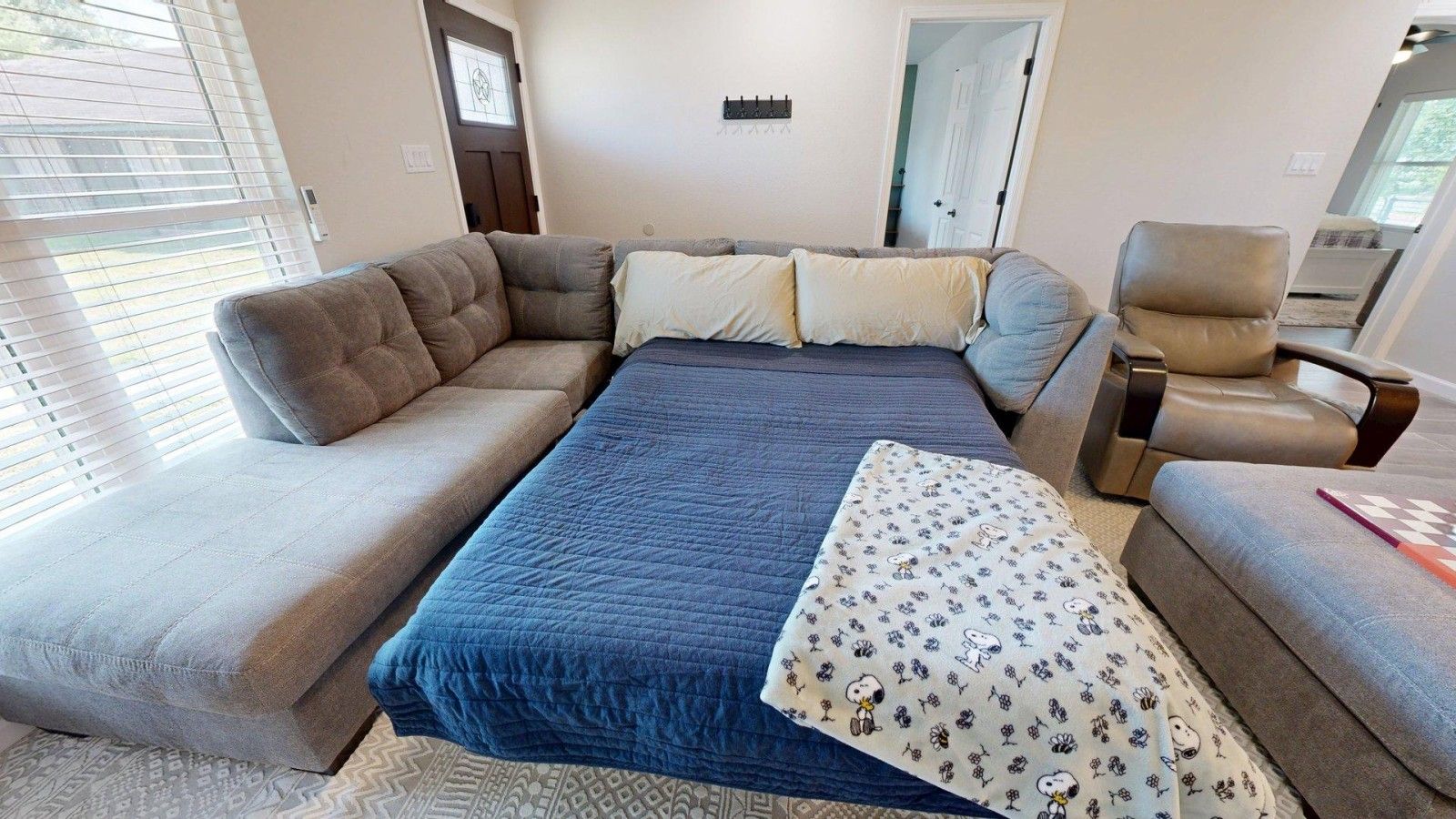 A room with a large bed, a sofa, a chair, and a patterned throw.