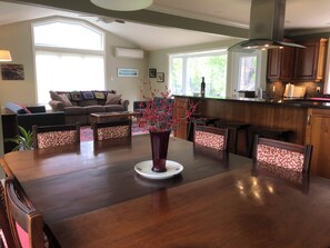 A dining area with a wooden table, chairs, and a vase with red flowers. There is a kitchen in the background with wooden cabinets and a window. - Fredericton Home Close to Downtown in Peaceful Neighbourhood (Fredericton)