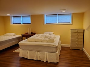 A bedroom with two beds, a dresser, a nightstand, and two windows with blinds. - Fredericton Home Close to Downtown in Peaceful Neighbourhood (Fredericton)