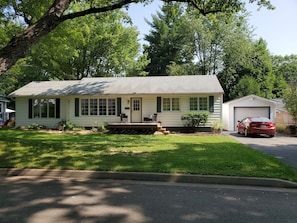 A single-story house with a front porch, a garage, and a red car parked in the driveway. - Fredericton Home Close to Downtown in Peaceful Neighbourhood (Fredericton)