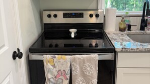 Una cocina con un microondas Whirlpool de acero inoxidable, una estufa negra con reloj digital y una ventana con vista a árboles.