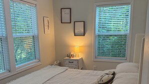 Un dormitorio con cama, mesita de noche, lámpara y dos ventanas con persianas.